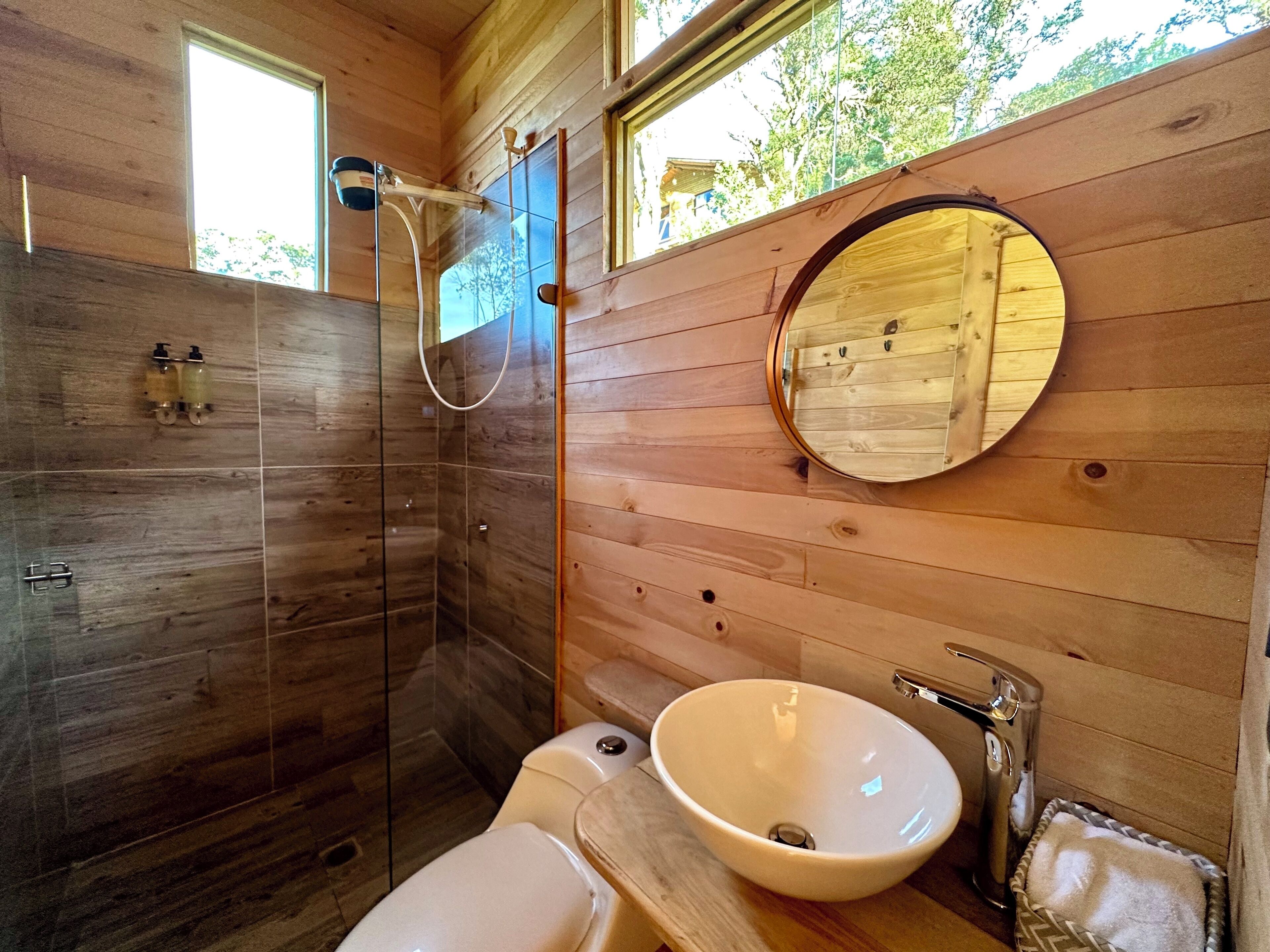 A wooden interior bathroom with a glass-enclosed shower, a round mirror, and a white sink.