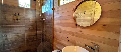 A wooden interior bathroom with a glass-enclosed shower, a round mirror, and a white sink.