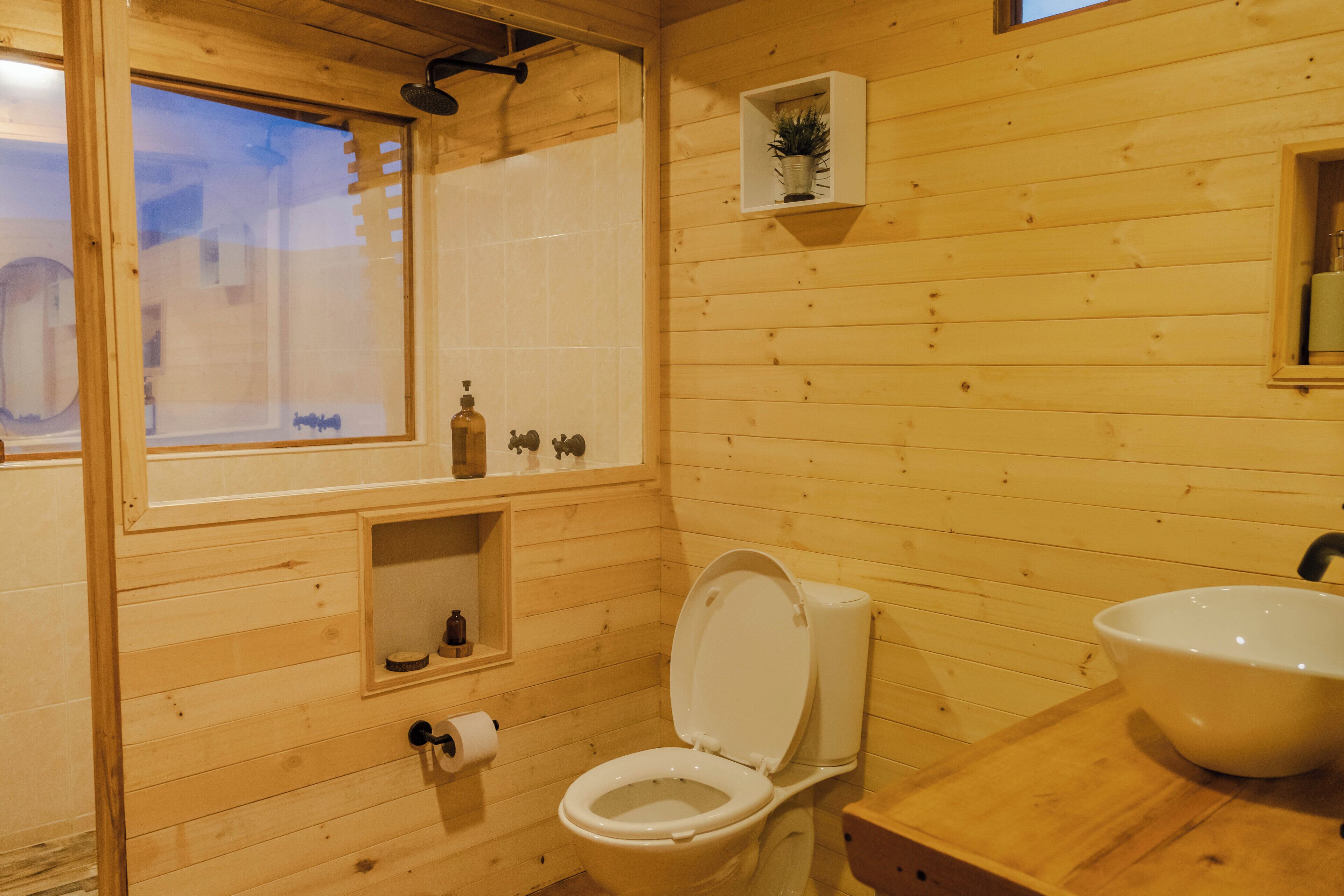 A wooden cabin bathroom with a toilet, sink, and a small shelf with toiletries.