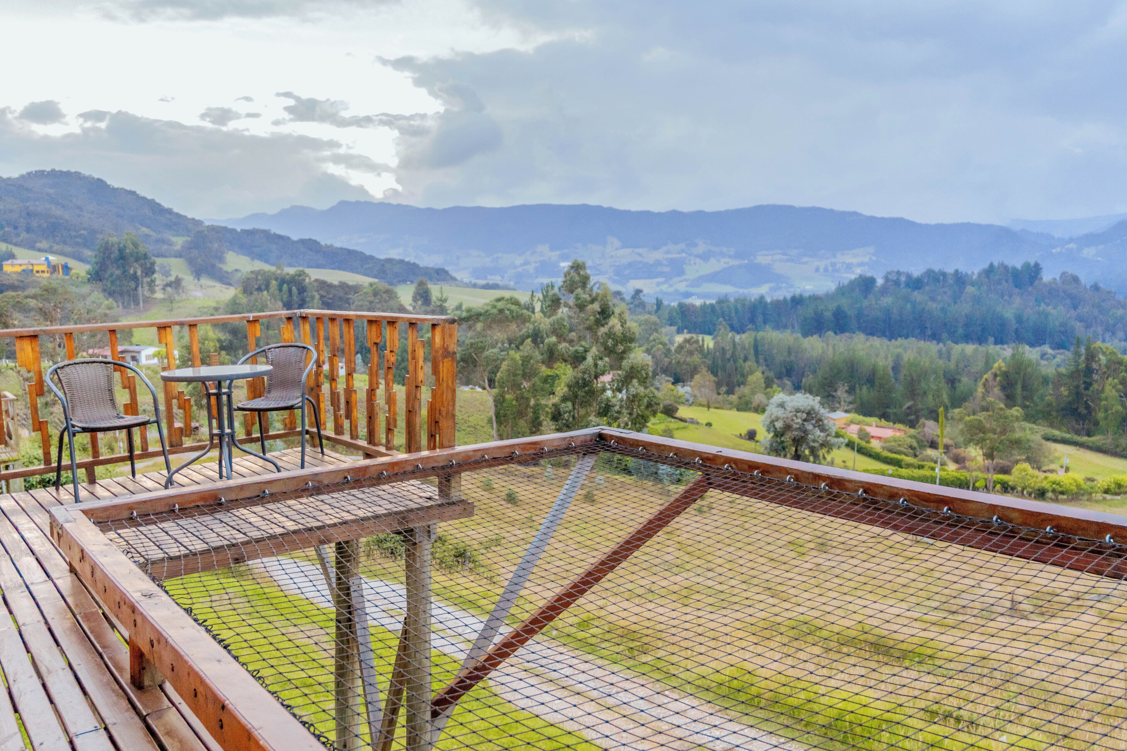 A wooden deck with a table and chairs, overlooking a mountainous landscape.