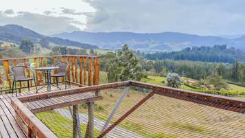 A wooden deck with a table and chairs, overlooking a mountainous landscape.
