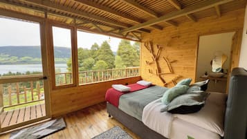 A wooden cabin with a bed, a window, and a view of a lake.
