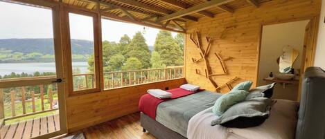 Una cabaña de madera con una cama, un ventanal y vistas a un lago.