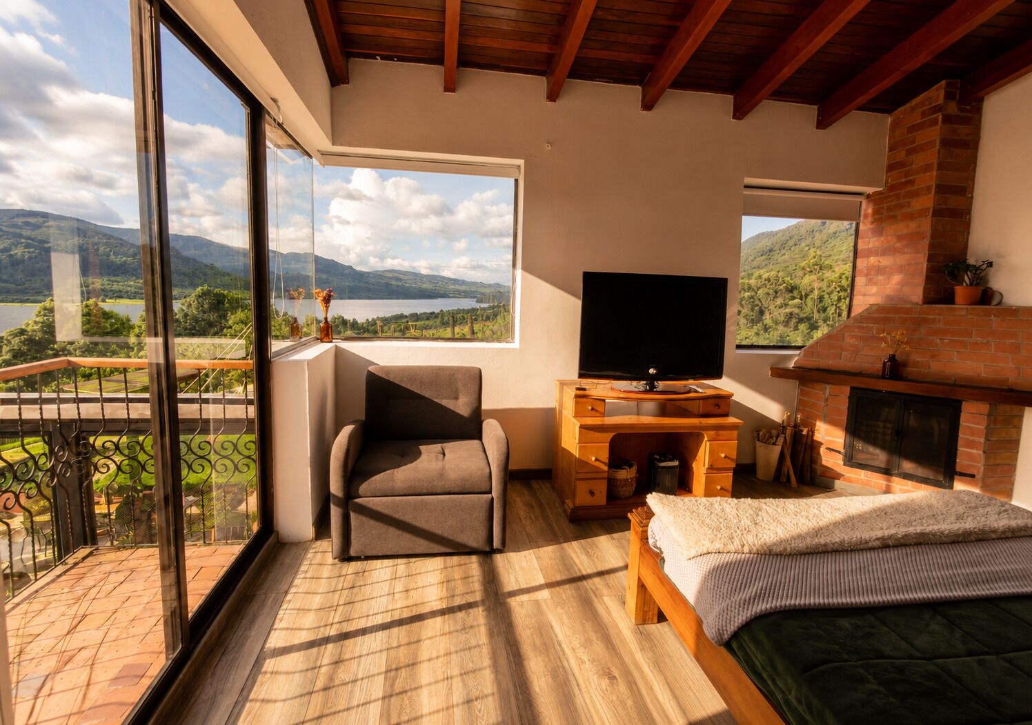Un dormitorio con una ventana grande, televisión, chimenea y balcón con vistas al paisaje.