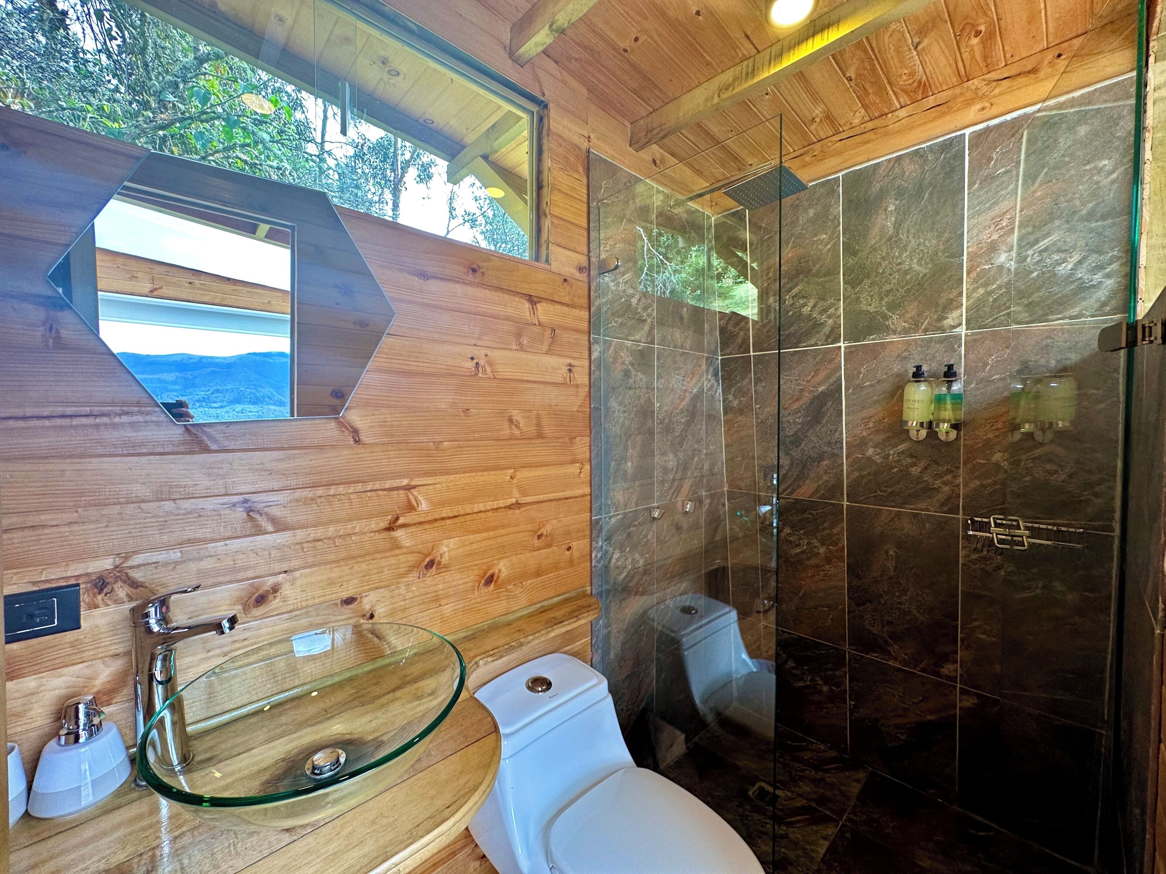 Ein modernes Badezimmer mit einem Waschbecken aus Glas, einer Toilette und einer Duschkabine mit Glastür.