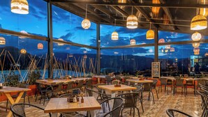 An outdoor dining area with tables and chairs, large windows, and hanging lights. - Neusa Hills Eco Hotel Boutique (Tausa)
