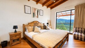 A bedroom with a wooden bed, a nightstand, a chair, and a large window with a view. - Neusa Hills Eco Hotel Boutique (Tausa)