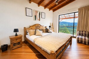 Une chambre à coucher avec un lit en bois, une table de chevet, une chaise et une grande fenêtre donnant sur un beau paysage.