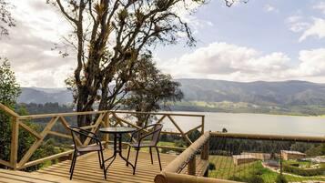 Um deck de madeira com duas cadeiras e uma mesa, com vista para um lago e montanhas.