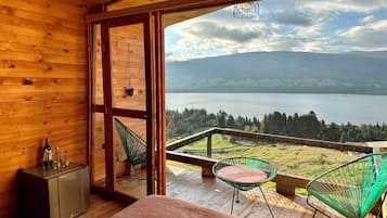 Une pièce de cabane en bois avec une grande fenêtre donnant sur un lac et des montagnes.