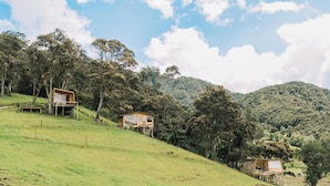 A hillside with wooden cabins, surrounded by trees and hills. - Neusa Hills Eco Hotel Boutique (Tausa)