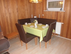 A dining area with a table set for four, surrounded by chairs, in a room with wooden walls and a radiator.