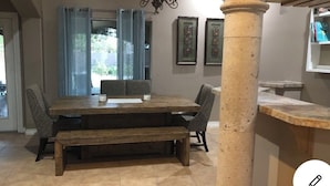Ein Essbereich mit einem Holztisch, Bänken und Stühlen. Über dem Tisch hängt eine Chandelüster, im Vordergrund steht eine große Säule.