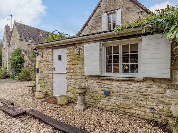 A stone house with a white door and window shutters, a gravel driveway, and a stone wall. - Kilcot Coach House is a detached cottage within the frounds of Kilcot House. (Lower Kilcot, near Wotton-under-Edge)