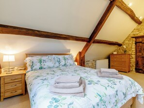 A bedroom with a bed, wooden headboard, a nightstand, a lamp, a dresser, and a stone wall.