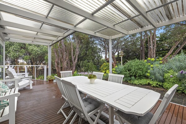 A covered outdoor patio with a white table and chairs, surrounded by lush greenery and trees. - ASCALON COTTAGE STYLE HOLIDAY RETREAT, SORRENTO (Sorrento)