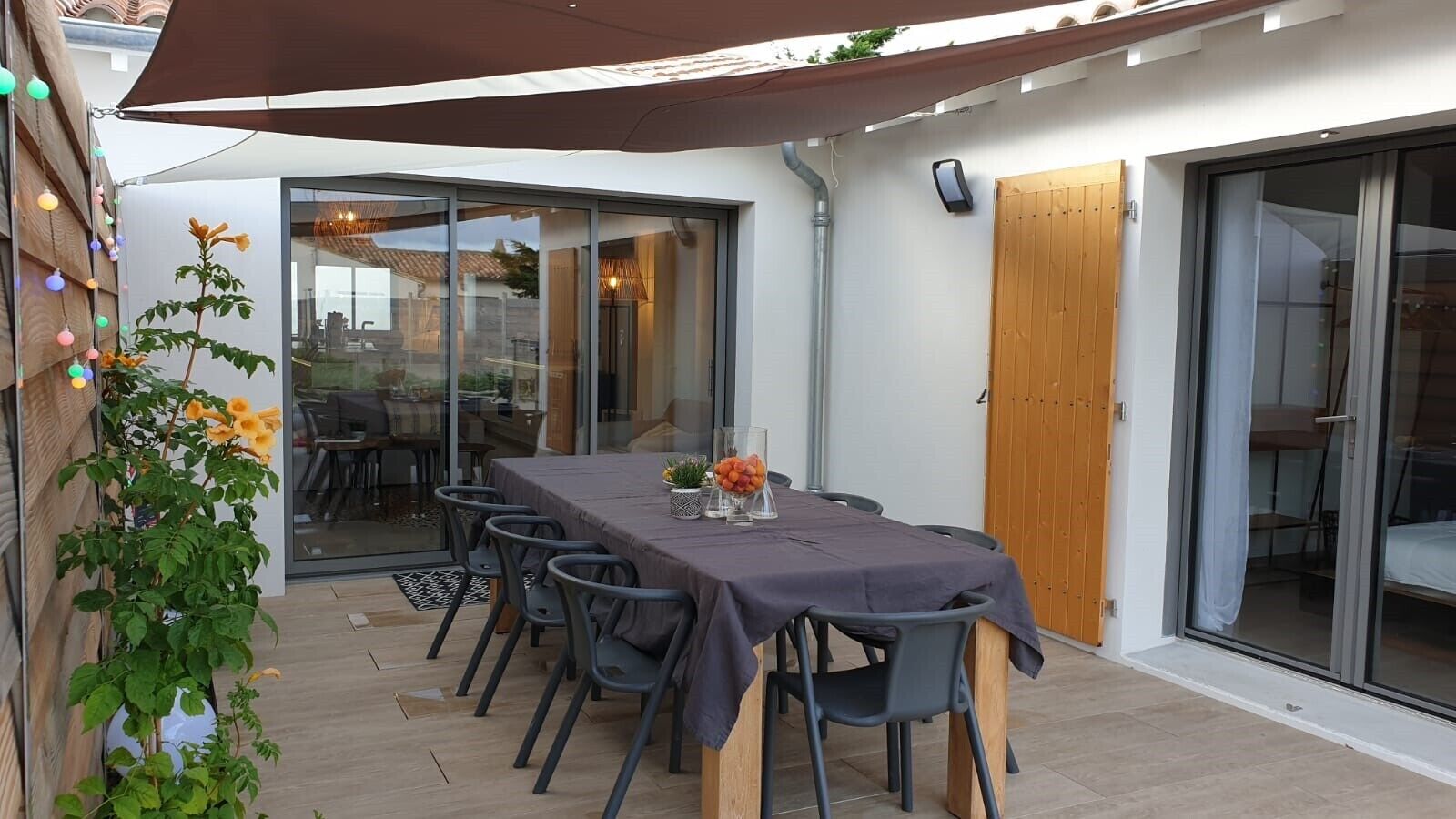 An outdoor dining area with a table and chairs, a pergola, and a view into the house.