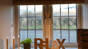 A window with a view of a rural landscape, a potted plant, and wooden letters spelling "RELAX" on a windowsill.
