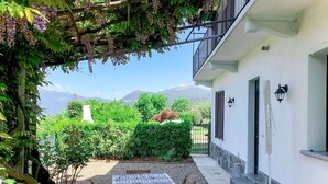 Un patio con una mesa y sillas, un edificio blanco de base de piedra, y montañas al fondo.