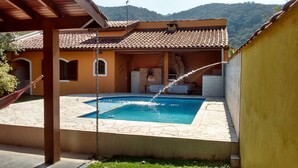A swimming pool with water jets, a hammock, and a covered patio area. - House for Season in closed condominium (Caraguatatuba)