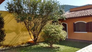 A building with a yellow facade and a tiled roof, surrounded by a well-maintained lawn and trees. - House for Season in closed condominium (Caraguatatuba)