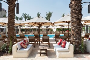 Un área junto a la piscina con sillones de descanso, sombrillas y una piscina.