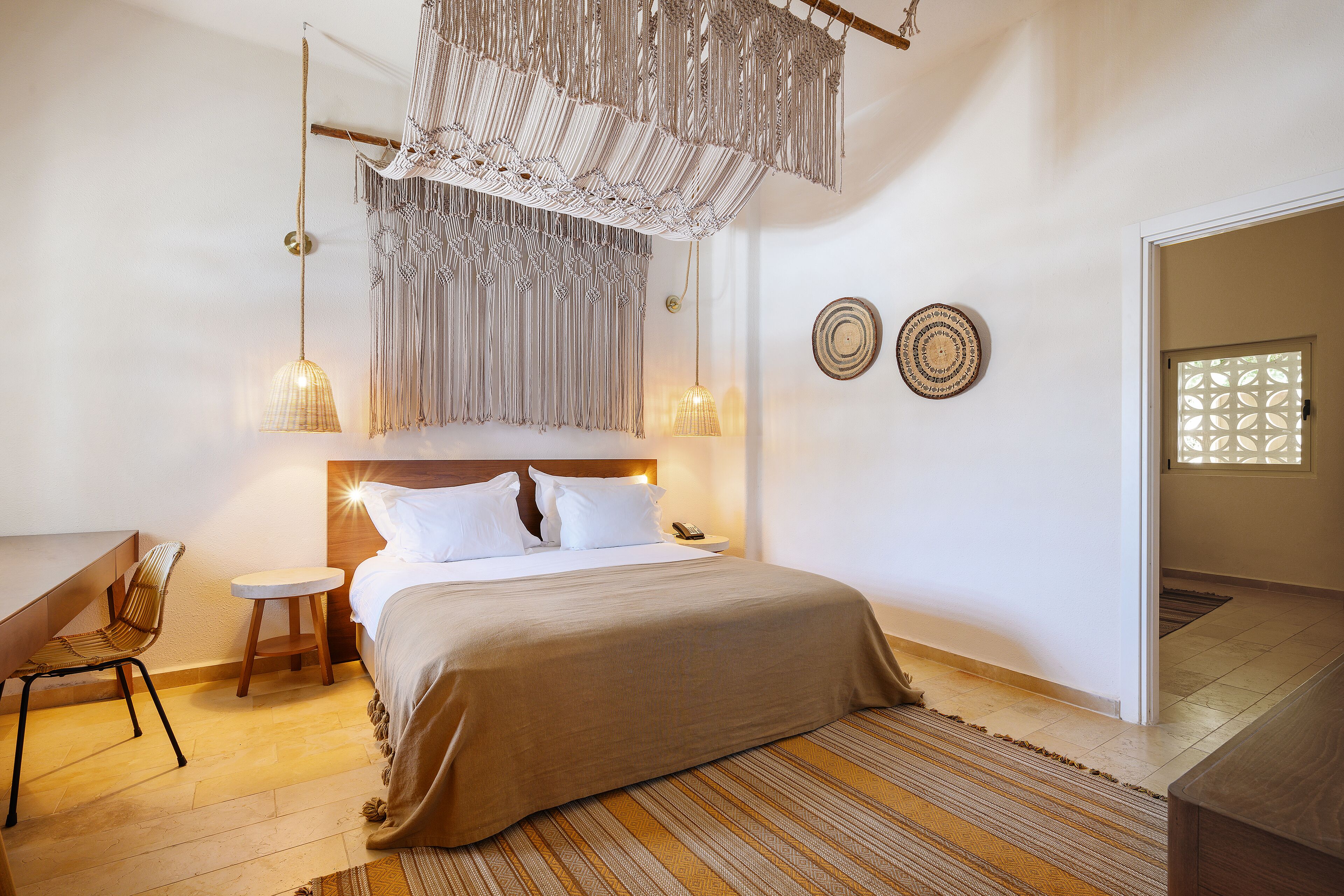 Un dormitorio con cama, mesita de noche, silla, macramé colgante y decoración en la pared.