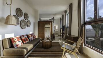 Un salon moderne avec un canapé, une table basse et un fauteuil. De grandes fenêtres offrent une vue sur les palmiers à l’extérieur.