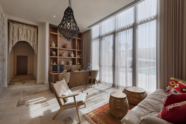Un ampio soggiorno con una grande finestra, una scrivania in legno, un divano confortevole e un arazzo decorativo in macramè.