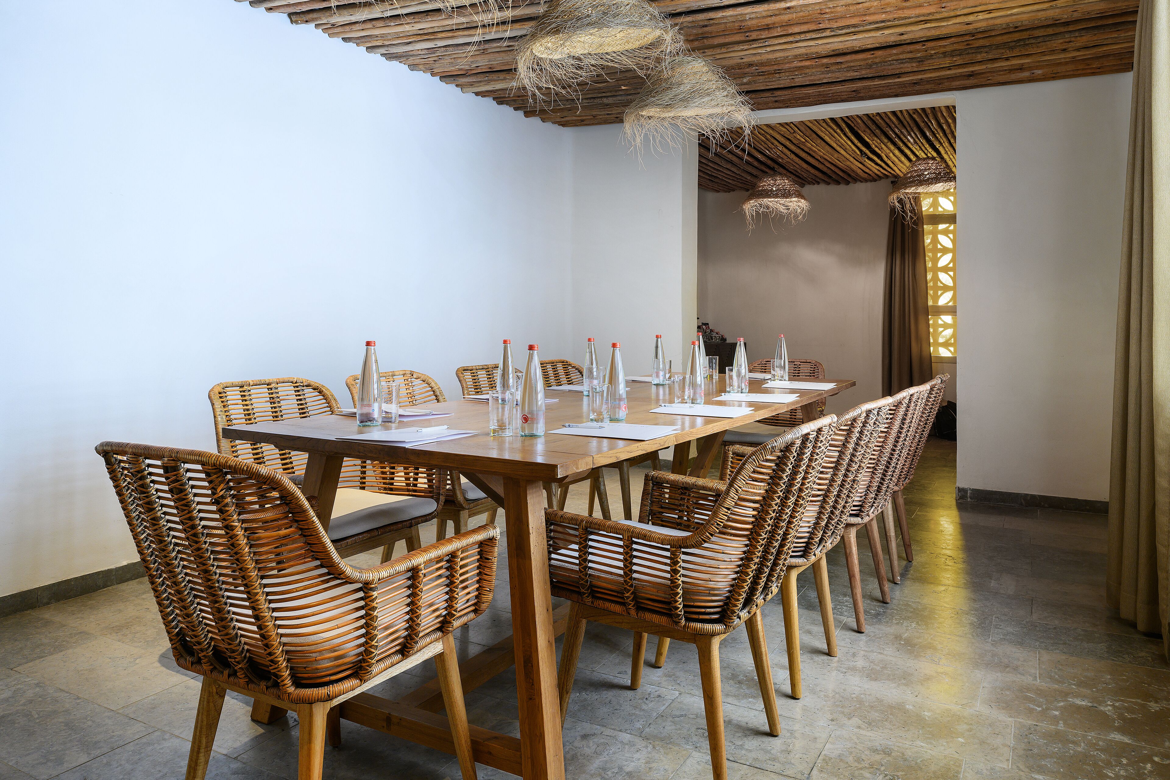 A dining area with a long wooden table, wicker chairs, and hanging light fixtures.