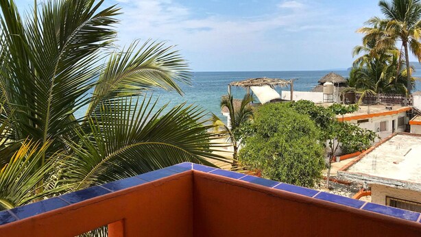 Un balcone con vista sul mare, una struttura con tetto di paglia e palme.