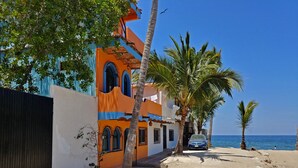 Un edificio sul lungomare con facciata blu e arancione, palme e una vista libera sul mare.