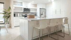 A modern kitchen with white cabinetry, stainless steel appliances, and a central island with bar stools. - Luxury Villa Miami Shores (Miami Shores)