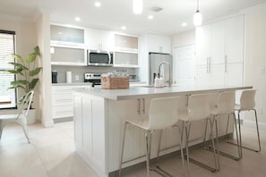 A modern kitchen with white cabinetry, stainless steel appliances, and a central island with bar stools.