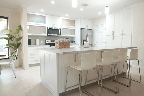 A modern kitchen with white cabinetry, stainless steel appliances, and a central island with bar stools.