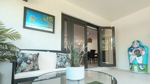A modern living room with a glass coffee table, a white sofa with patterned cushions, a potted plant, and a large window. - Luxury Villa Miami Shores (Miami Shores)