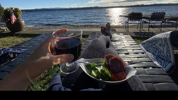 Um terraço à beira-mar com vista para o oceano, uma mesa com um prato de comida e um copo de bebida.