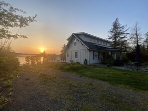 A house with a porch and a view of the sunset over a body of water. - Olympia Waterfront Beach Cottage (Olympia)