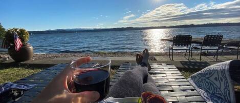Une terrasse au bord de l’eau avec vue sur l’océan, une table avec une assiette de nourriture et un verre rempli de boisson.