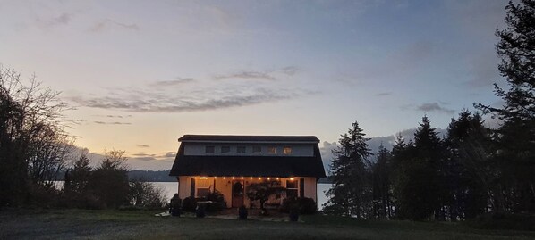 A two-story building with a flat roof and a balcony, surrounded by trees and a body of water in the background. - Olympia Waterfront Beach Cottage (Olympia)