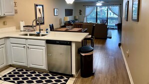 A kitchen with a dishwasher, a sink, and a trash can. There is a dining area with a table and chairs. - Newly Renovated Home away from Home...Sandcastle Beach #43 (Navarre)
