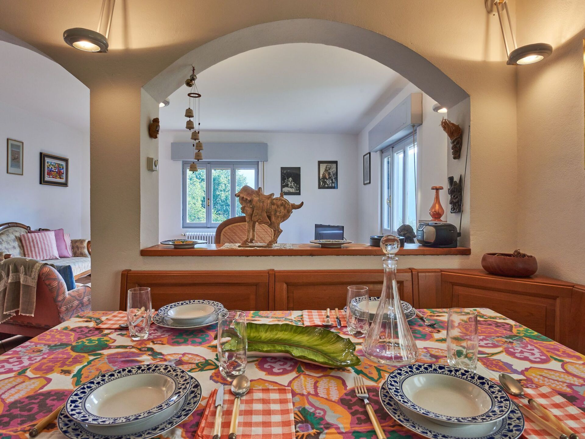 A dining area with a table set for four, a decorative hanging, and a view of the living room through an archway.