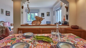 Un coin repas avec une table dressée pour quatre personnes, une décoration murale et une vue sur le salon, accessible par une arche.
