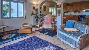 Un salon confortable avec un canapé, un fauteuil, une petite table et une vue sur la cuisine.