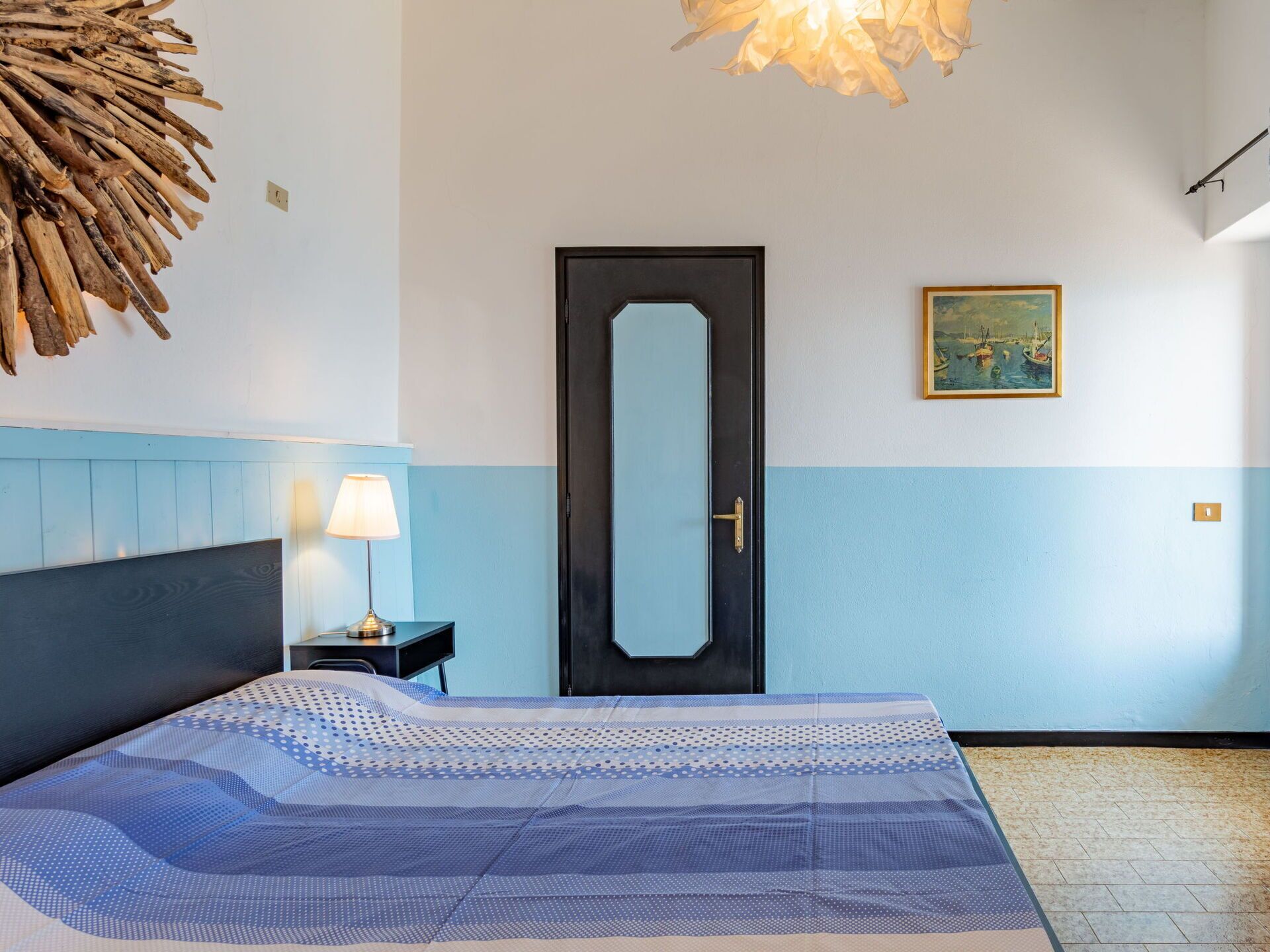 A room with a bed, a nightstand, a lamp, a door, and a painting on the wall.