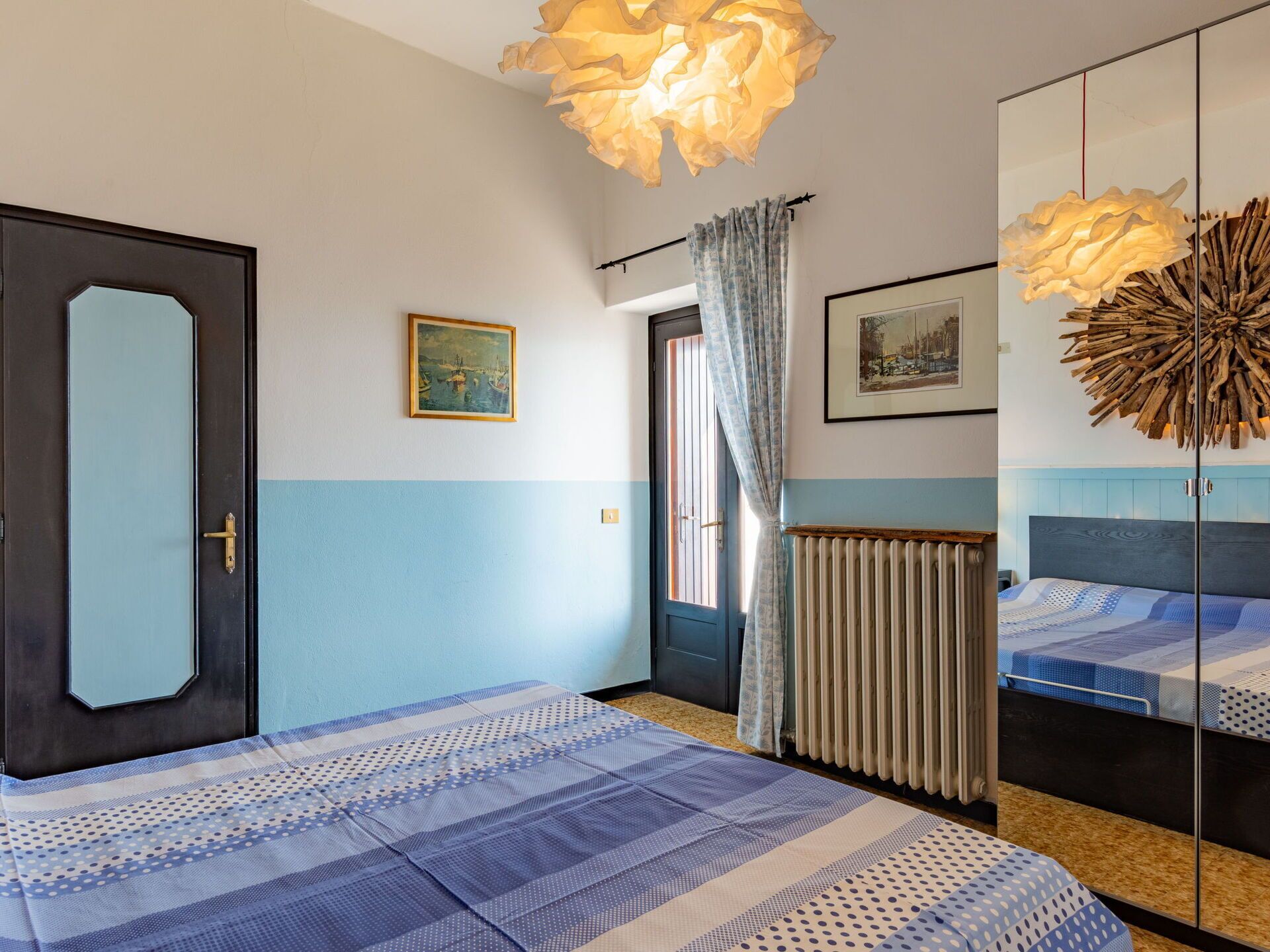 Een slaapkamer met een bed, een radiator, een raam met gordijnen en een schilderij aan de muur.
