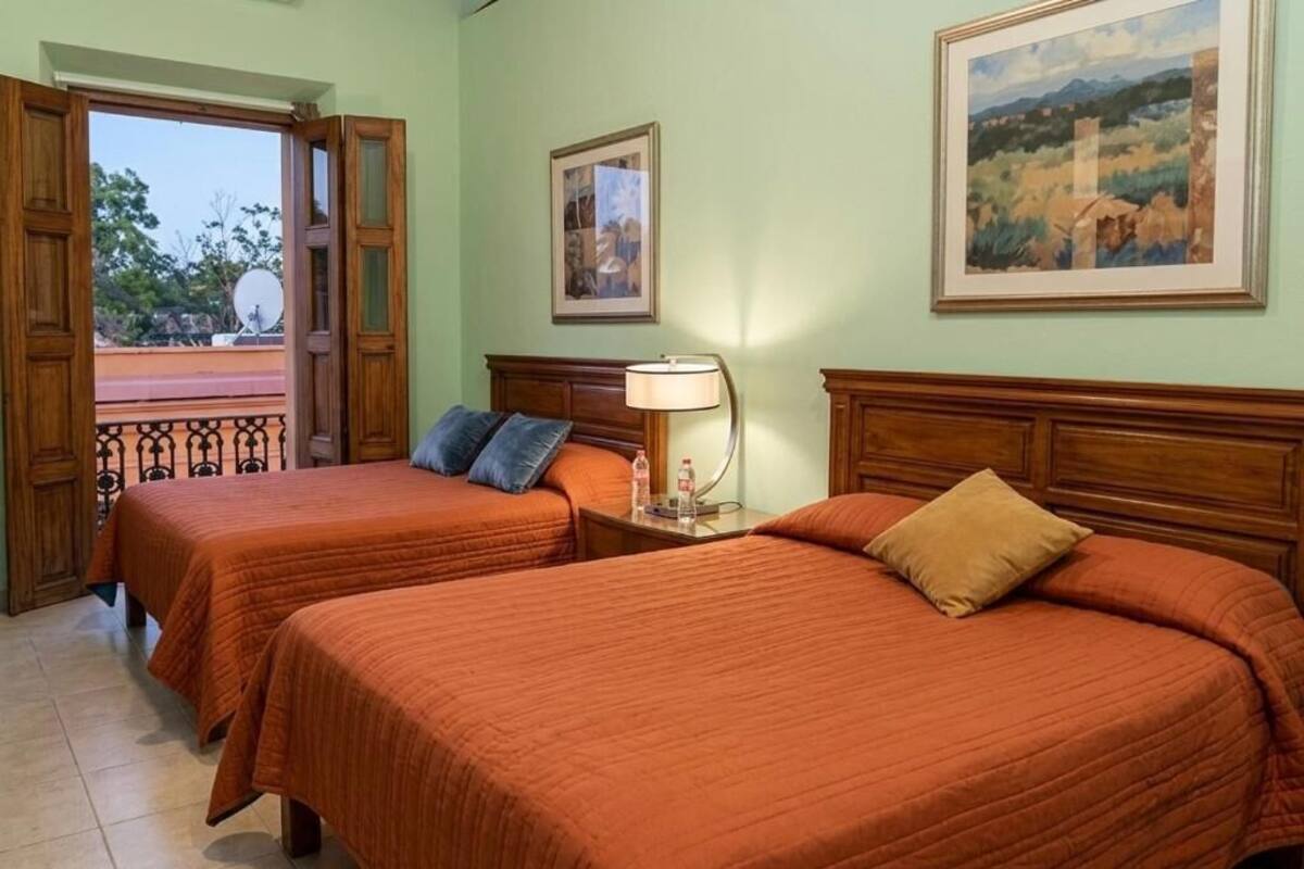 A room with two beds, a nightstand, a lamp, and a painting on the wall.