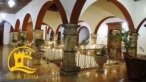 Un vestíbulo amplio con techos altos en arco y suelo pulido, que destaca por una columna central y plantas en macetas.