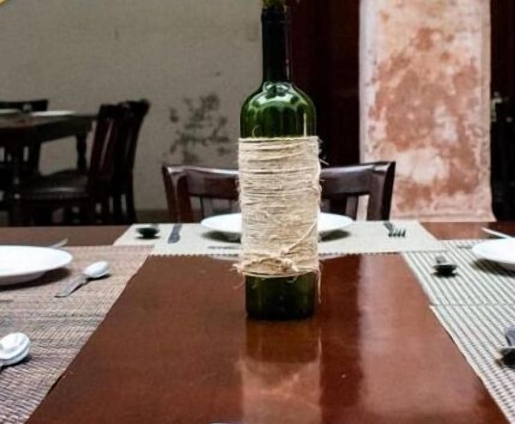 Een eettafel met een groene fles omwikkeld met touw, omringd door borden, bestek en placemats.