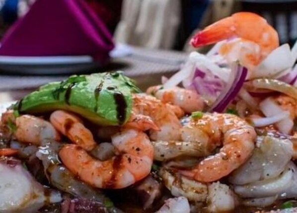 Primer plano de un plato de mariscos con camarones, aguacate y cebollas.